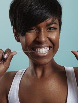 Smiling woman flossing to prevent dental emergencies