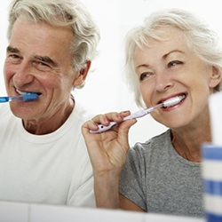 senior man and woman brushing their teeth together 