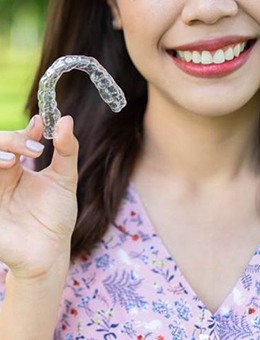 Woman smiles outside while holding Invisalign clear aligner