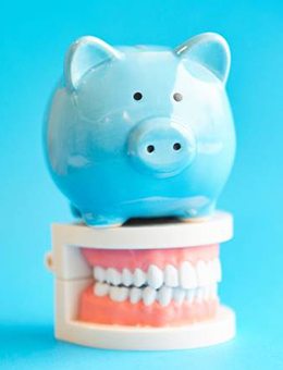 Piggy bank on model teeth representing the price of Invisalign