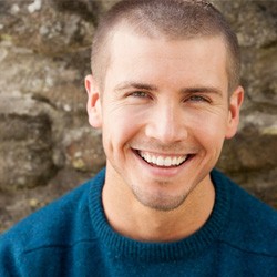 Man in blue shirt smiling in front of brick wall