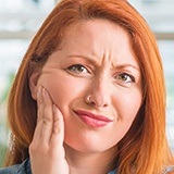 Red haired woman holding jaw in pain before emergency dentistry treatment