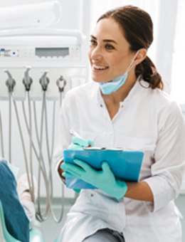 Dentist smiling while taking notes and talking to patient