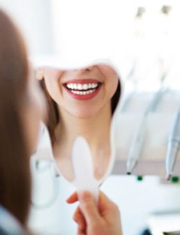 Woman with white teeth smiling in tooth-shaped mirror